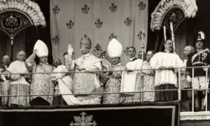 Uroczysta procesja z papieżem w tiarze, jego nakrycie głowy jest bogato zdobione. W tle inni duchowni i wierni.