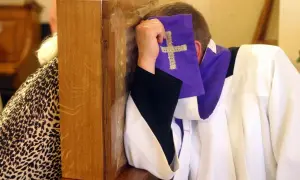 Spowiedź w konfesjonale. Czy nie pójście do kościoła w niedzielę to grzech ciężki? Duchowny w białej albie i fioletowej stulejce z krzyżem.