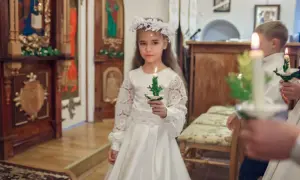 Dziewczynka w białej sukni i wianku trzyma świecę. To ważny moment, w jakim wieku komunia.