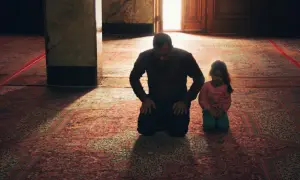Ojciec i córka klęczą na dywanie, pogrążeni w modlitwie o spokój w rodzinie.