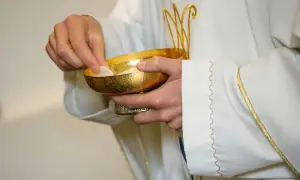 Kapłan podaje hostię z kielicha. Poważne grzechy po których nie można przystąpić do komunii wymagają spowiedzi.