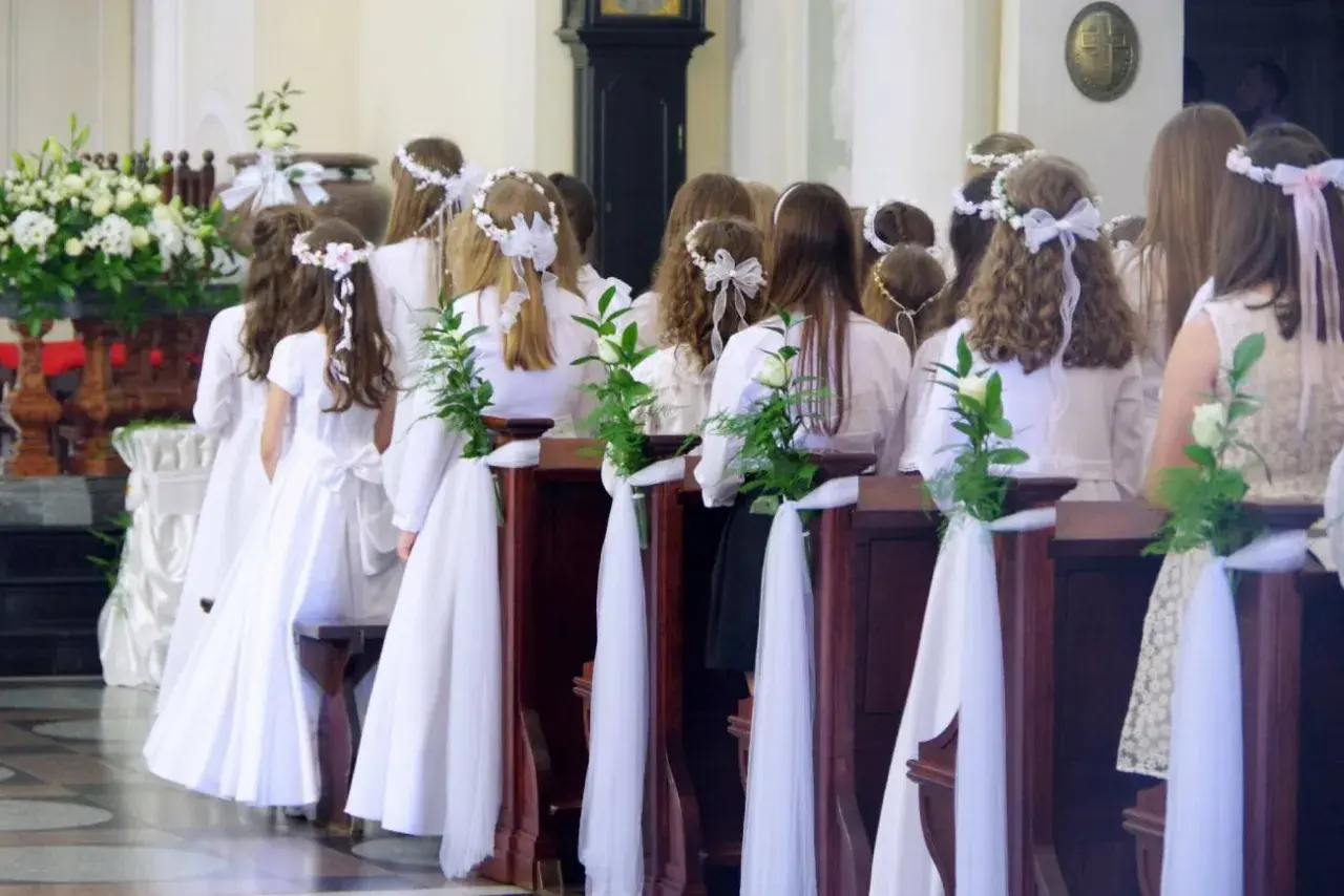 Dzieci w białych strojach, ozdobione wiankami, czekają na komunię. Zazwyczaj do komunii idzie się w wieku około 8-9 lat.