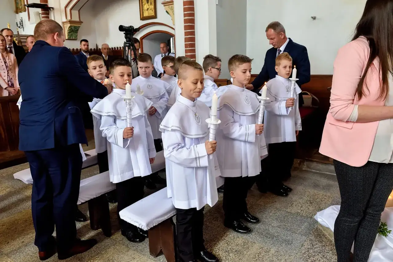 Chłopcy w białych albach, trzymający świece, czekają na uroczystość. W jakim wieku idzie się do komunii? Zazwyczaj w wieku około 9 lat.